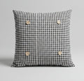 A black and white gingham square button pillow on a bed with white bedding.