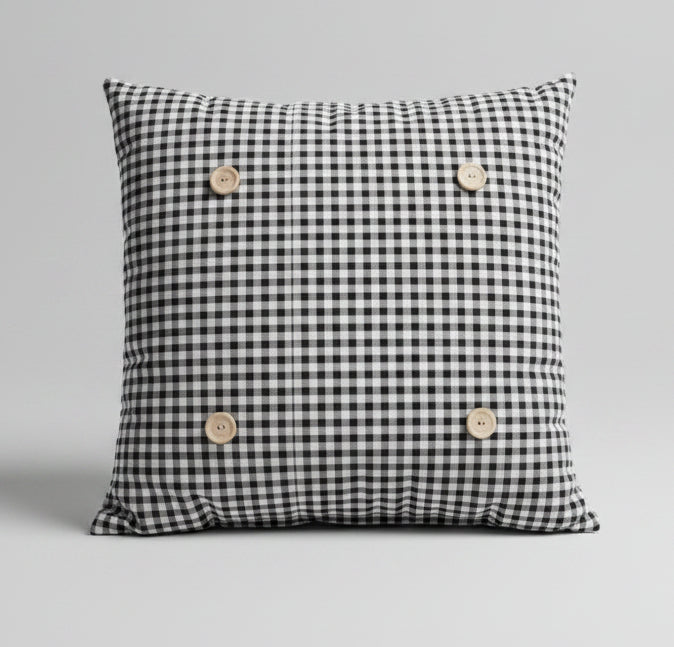 A black and white gingham square button pillow on a bed with white bedding.