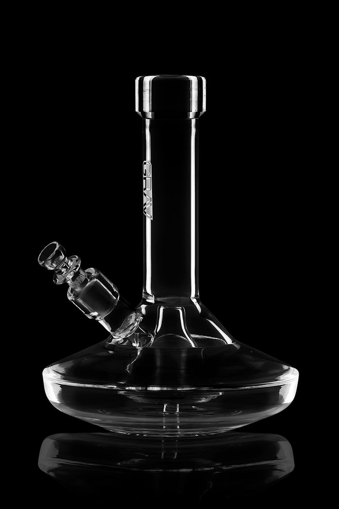 Clear glass water pipe (bong) with ice catch and angled downstem, reflecting on a glossy surface.