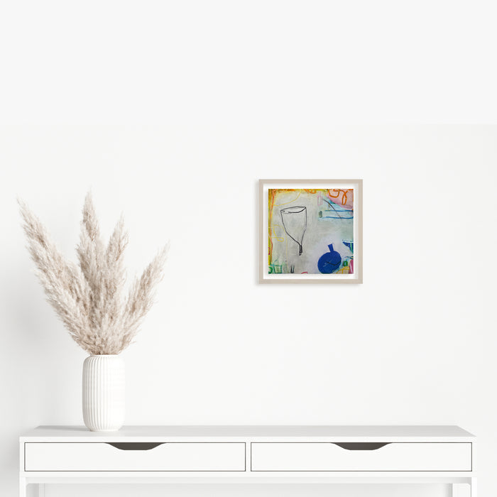 The artwork 'LS no. 12' by Janice La Motta features a minimalist still life composition with a delicate gray wine glass and vibrant blue vessel against a soft pastel background. Created with oil pastel on Yupo paper, the piece showcases loose, gestural strokes and gentle color transitions, measuring 9x9 inches in a white frame.
